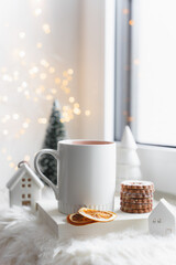 Eine weiße Tasse Tee und Kekse auf einem Buch an einem Fenster. Lichterkette, hell, Weihnachten.