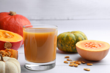 Tasty pumpkin juice in glass and different pumpkins on white wooden table