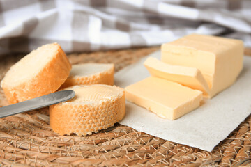 Tasty cut baguette with fresh butter on wicker mat, closeup