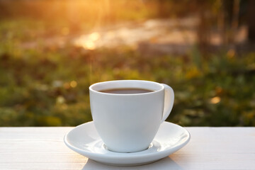 White cup with coffee on wooden table in morning outdoors