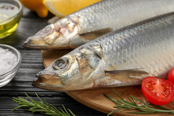 Delicious salted herrings and ingredients on black wooden table, closeup
