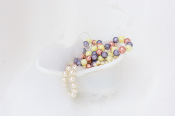White bath full of foam full of jewelry made of multi-colored beads. Copy space.
