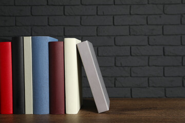 Fototapeta na wymiar Many different hardcover books on wooden table near dark brick wall, space for text