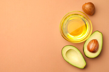 Cooking oil in bowl and fresh avocados on beige background, flat lay. Space for text