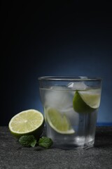 Glass of vodka with lime slices, mint and ice on grey table