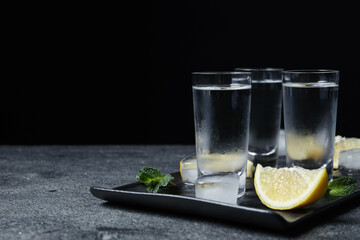 Shot glasses of vodka with lemon slices, mint and ice on grey table. Space for text