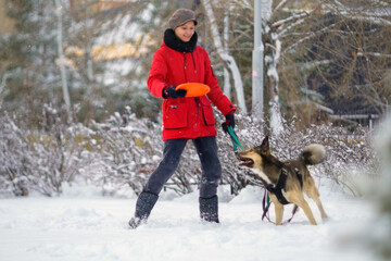 Fototapeta na wymiar Girl plays with a dog in winter, training a pet. Snowy winter street. Selective focus