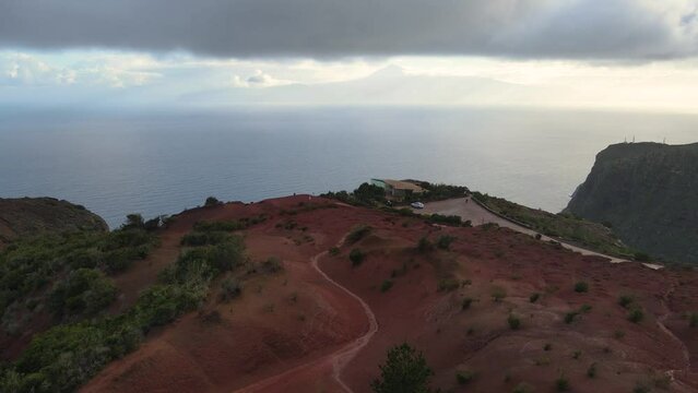Aerial view of stunning viewpoint Mirador de Abrante with glass observation balcony above Agulo village in La Gomera island at sunrise. Restaurant on red clay.