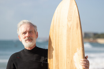 Portrait of aged surfer enjoying active rest in summer. Concentrated bearded man in wetsuit holding...