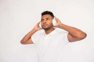 Dreaming young man listening to music in headphones. Male Indian model with brown eyes and curly hair in white polo shirt wearing headphones enjoying music. Lifestyle, music concept