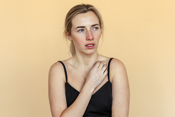 Fototapeta premium Portrait of the thoughtful upset woman standing over beige background, lost in thoughts. Pensive unhappy girl feeling lonely and depressed, thinking about relationship or personal problems