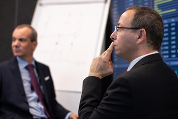 Portrait of corporate analyst listening to financial reports. Two concentrated men monitoring market charts on big screen and making data analysis in office. Business analysis and strategy concept