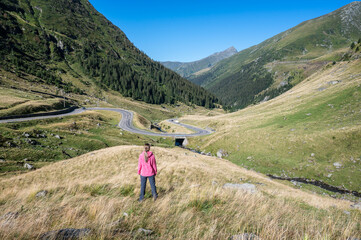 Obraz premium Rear view of a young woman standing at the famous picturesque curvy road in Fagaras mountain Romania. Beautiful girl enjoying the beauty of nature.