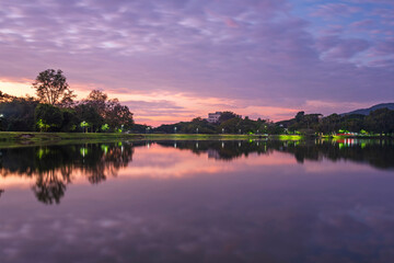 The cloud and trees on water reflection in the beautiful sunrise at Ang Kaew of Chiangmai University, and there is a relaxing break for exercisers and tourists