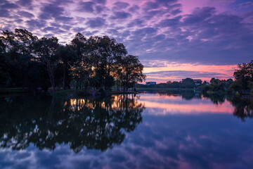The cloud and trees on water reflection in the beautiful sunrise at Ang Kaew of Chiangmai University, and there is a relaxing break for exercisers and tourists