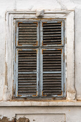 Old window with worn wooden shutters on exterior wall of an old ruined house