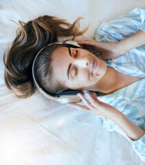 Top view, woman and headphones in bedroom, morning and relax with mental health podcast, mindfulness audio and zen music. Face of happy, calm and peaceful girl listening to radio, sound and wellness