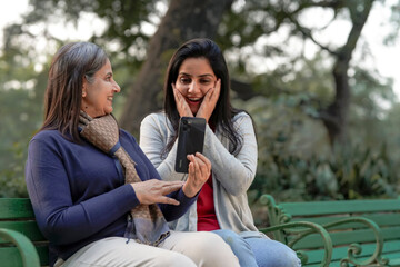 Two indian woman in warm wear and talking on video call at park.