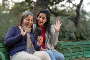 Two indian woman in warm wear and talking on video call at park.