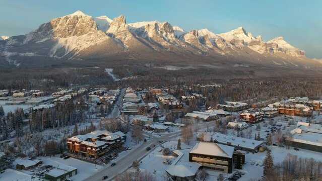 The amazing Canadian Rockies peer over the quaint town of Canmore Alberta. Golden hour sun hits the peaks. Aerial.