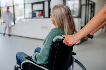 Fototapeta na wymiar Rear view of hospital worker pushing senior woman on wheelchair.