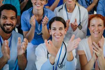 Portrait of happy doctors, nurses and other medical staff clapping in hospital.