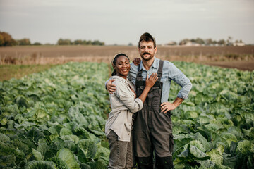 Portrait of a smiling multiracial couple standing in a working outfit in the field, small family business concept