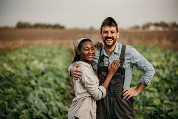 Portrait of a smiling multiracial couple standing in a working outfit in the field, small family business concept