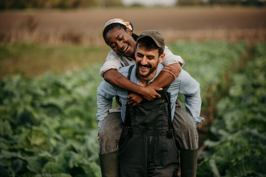 Man and woman field workes having fun and a piggyback ride during a workday on the farm.