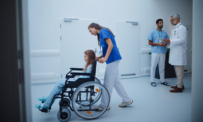 Young nurse pushing little girl on wheelchair at hospital corridor.