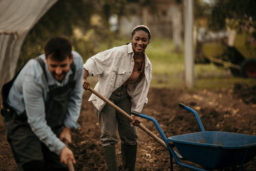 Man and woman in 20s and 30s pausing to discuss progress and compost in smallholding vegetable...