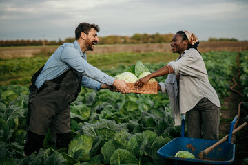 Shot of an attractive young female and male farmers in working clothes carrying a crate of fresh produce.