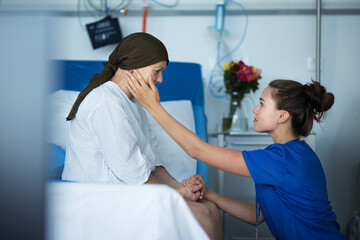 Empathic nurse taking care of senior woman with cancer, stroking her cheek.