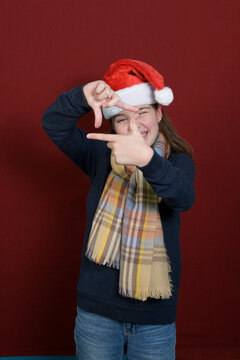 A girl in a santa hat shows a gesture - a symbol of a photo film. Dark red background. Vertical