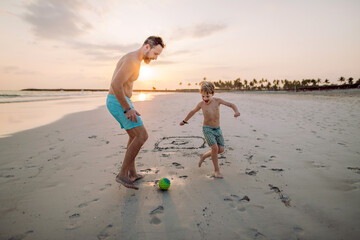 Father with his son plaing football on the beach. - obrazy, fototapety, plakaty