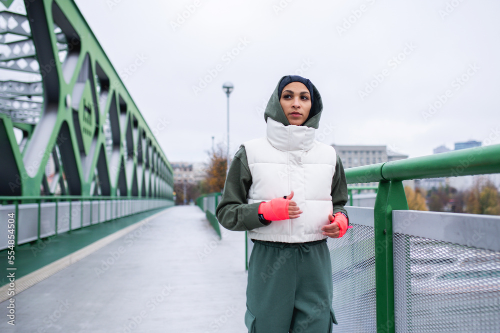 Wall mural young muslim woman running outdoor in city.