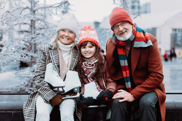 Portrait of seniors and their granddaughter in winter at outdoor ice skating rink.