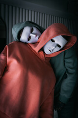 Portrait of two people in white theatrical masks and hood on black background. Concept of mental...