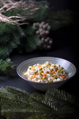 a traditional New Year's salad in a plate stands on a black background, fir branches lie nearby