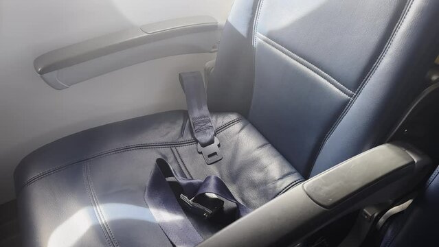 Empty plane window seat with unbuckled seatbelt