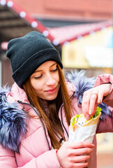 Street food. young woman holding greek meat gyros with tzatziki sauce, vegetables, feta cheese and french fries and eating oudoor winter