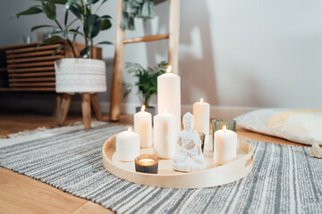 Wooden tray with burning candles and white Buddha statuette on the floor of modern Scandi interior. Zen Composition for meditation, yoga practice, relaxation. Balance and calm energy flow indoor