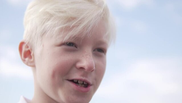 Close-up, of a blond boy's face against a blue sky.