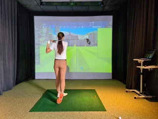 Poster Professional female golfer holding club playing golf indoors on golf simulator. © Nadzeya
