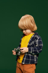 Portrait of little boy, child posing with vintage camera over green studio background. Photographer. Concept of childhood, emotions