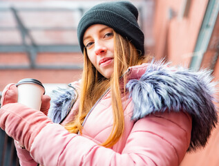 Young woman with cup of coffee in a hand on city street winter
