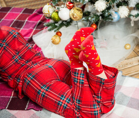 young woman in holiday pajamas laying down near christmas tree - 554867184