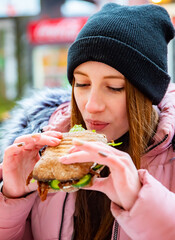 Street food. young woman holding juicy ciabatta sandwich and eating oudoor winter