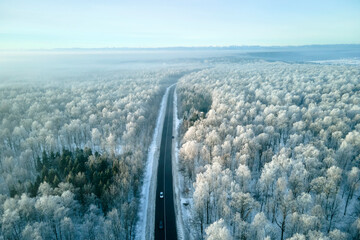 Aerial view of winter landscape with snow covered woods and black asphalt forest road on cold...