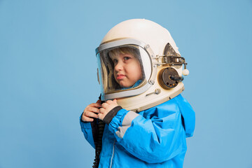 Portrait of little boy, child posing in astronaut costume, helmet over blue studio background....